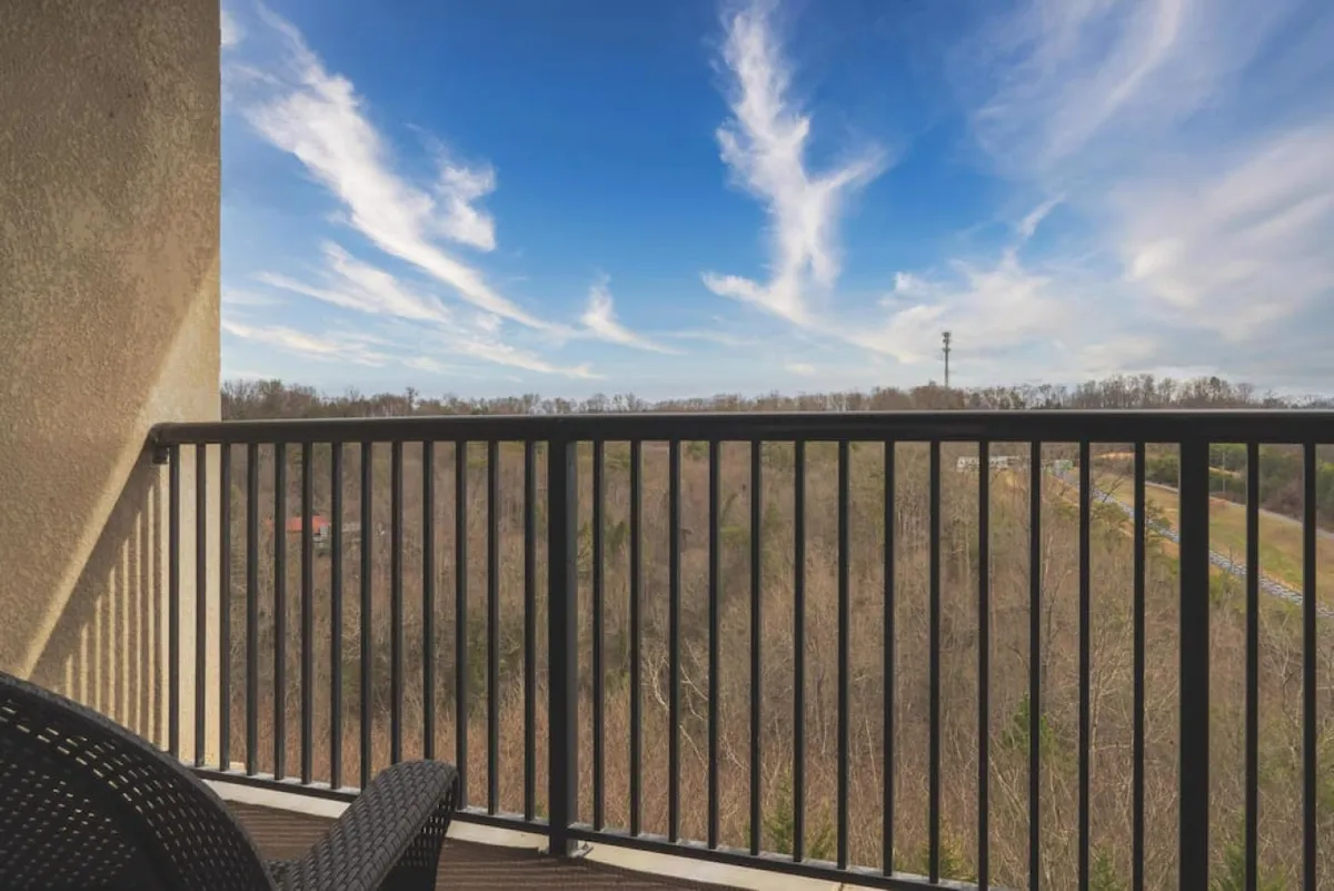 An expansive view of the landscape as seen from the condo's balcony, featuring a sky with wispy clouds and a balcony railing in the foreground. The tranquil scene invites guests to relax while overlooking the lush surroundings and distant mountains.