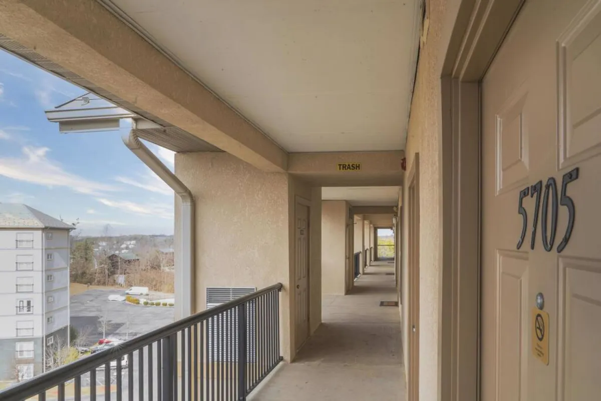 A casual, inviting corridor leading to the condo entrance, with the door number 5705 clearly visible. The scene also includes a balcony railing overlooking the area, subtly connecting indoor and outdoor elements and hinting at the community feel of the property.