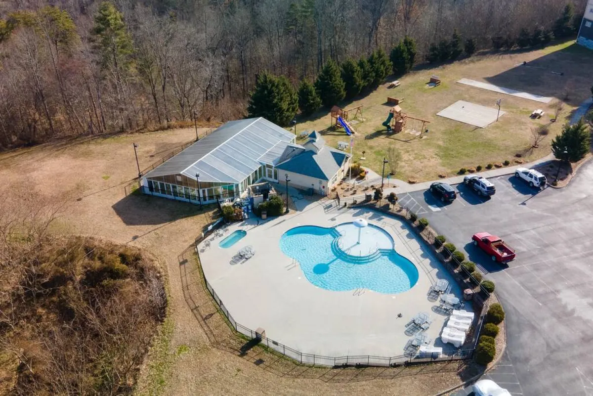 A vibrant outdoor scene featuring a sparkling swimming pool, a nearby playground where children are playing, and a well-maintained recreation area with seating and greenery. The building with large glass windows overlooks the amenities, suggesting easy access from the condo to the shared resort spaces.