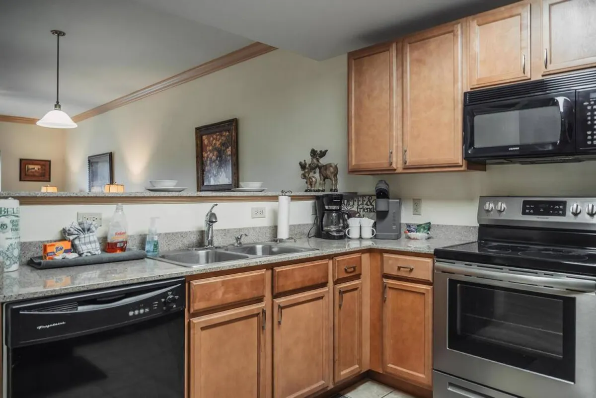 A bright and homey kitchen featuring stainless steel appliances, granite countertops, kitchen sink, wooden cabinets, and decorative items on the counter. The space looks ready for cooking, coffee brewing, and socializing.