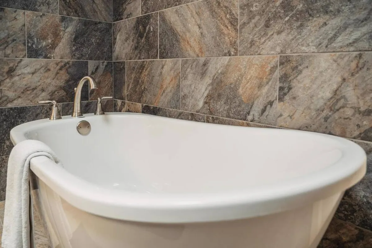 A serene bathroom featuring a freestanding bathtub, modern faucet, and textured wall tiles. The overall atmosphere is tranquil and inviting—a perfect setting for relaxation and self-care.