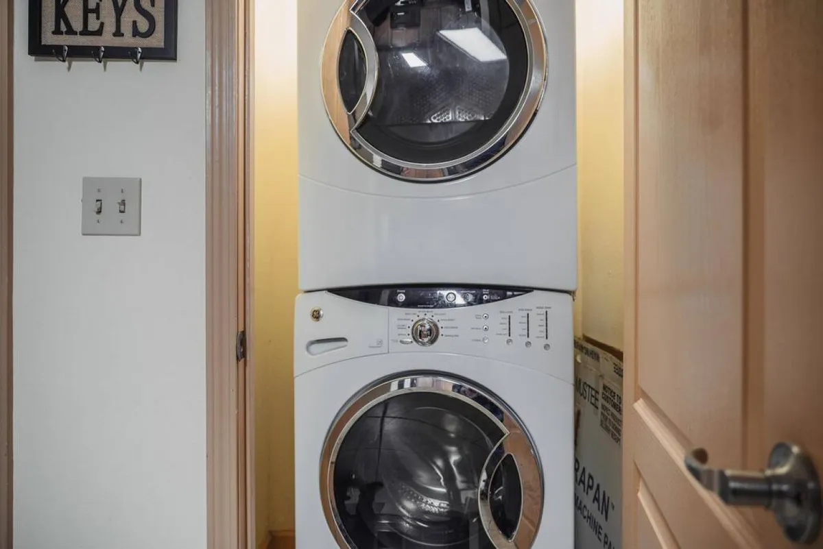 An in-unit laundry area featuring neatly stacked washer and dryer appliances, with a convenient keys holder on the wall. The space is practical and well-organized, emphasizing everyday convenience.