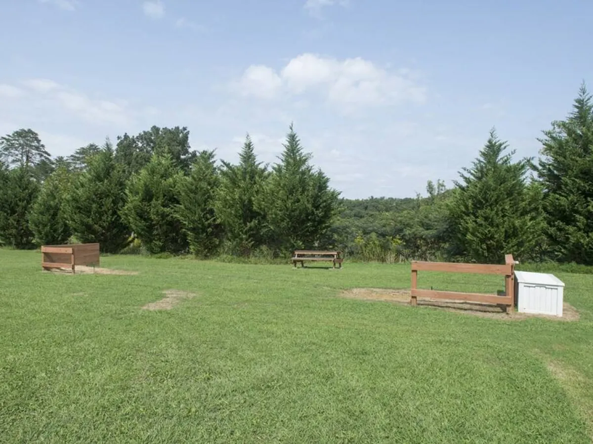 A peaceful outdoor area with wooden benches, lush green grass, tall trees, and hills in the background, ideal for relaxing, picnicking, or enjoying nature. The tranquil setting invites guests to unwind and experience the natural beauty of the resort grounds.
