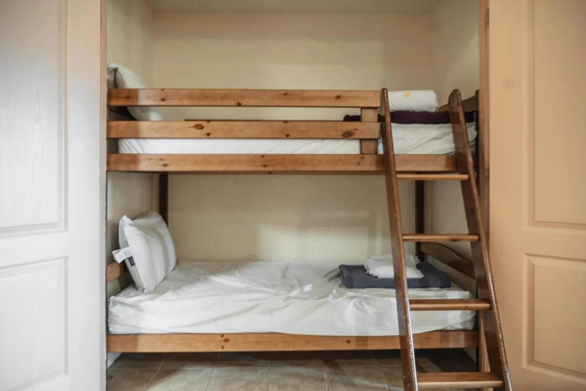 A cozy bunk bed setup with a wooden ladder and neatly made bed linens, inviting for children and perfect for sleepovers or sibling bonding. The space is functional yet playful, tucked into its own nook.