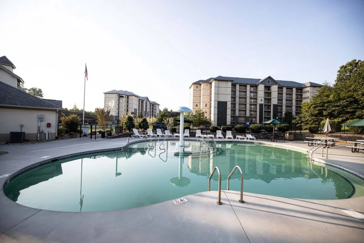 This exterior image showcases the resort's swimming pool, surrounded by lounge chairs and neighboring resort buildings. The inviting blue water hints at fun and relaxation, while the open layout highlights the communal, family-friendly atmosphere.